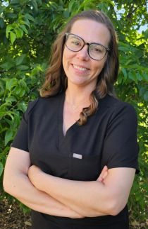 Annie Wood crossing arms and smiling in front of green leaves background